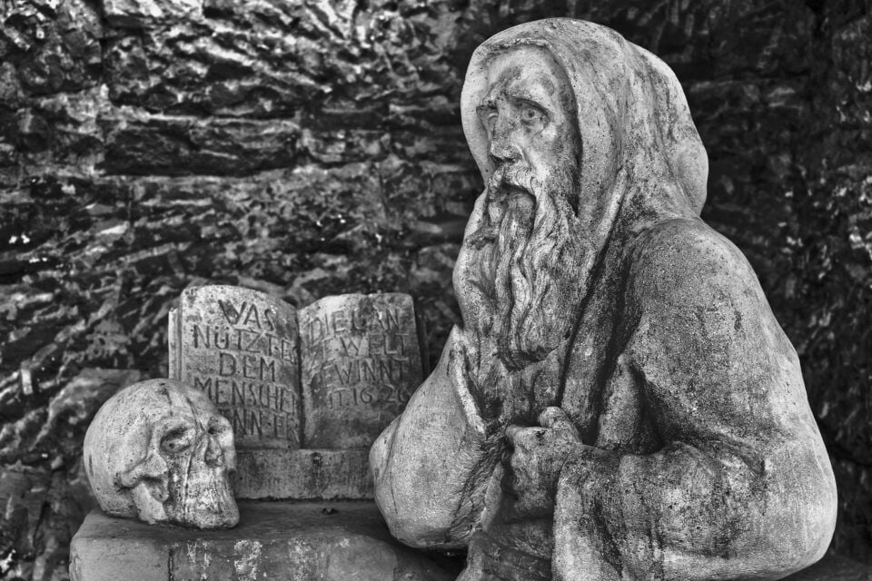 socha mnícha s knihou a lebkou