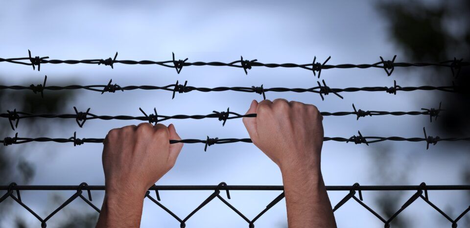 ruky na plote z ostnatého drôtu