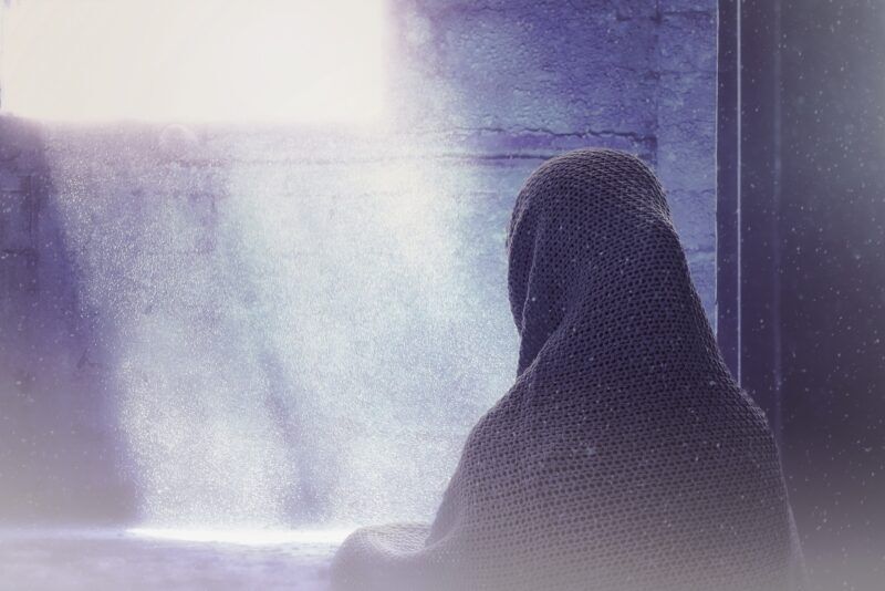 žena zozadu pod vlniakom sa pozerá z okna